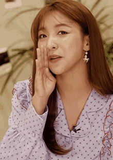 a woman wearing a polka dot shirt and earrings whispers into her hand