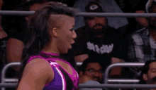 a woman in a purple and black wrestling outfit is making a funny face while standing in front of a crowd .