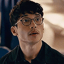 a man wearing glasses and a black shirt is looking up at the camera .