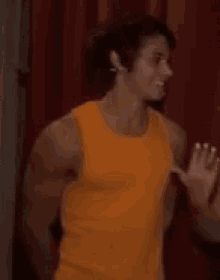 a man wearing an orange tank top is standing in front of a red curtain .