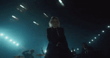 a woman is standing in front of a microphone on a stage with a band behind her
