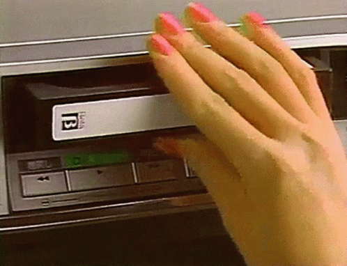 A retro clip of a woman's manicured hand inserting a VHS into a front-loading VCR.
