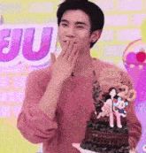 a young man in a pink sweater is holding a birthday cake .