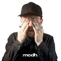 a man wearing glasses and a hat is covering his eyes with his hands and the word mcdh is above him