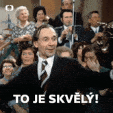 a man in a suit and tie is standing in front of a crowd and says to je skvely !