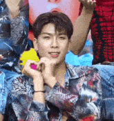 a young man is making a heart shape with his hands while sitting in front of a group of people .
