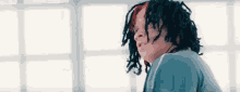 a man with dreadlocks is sitting in front of a window in a room .