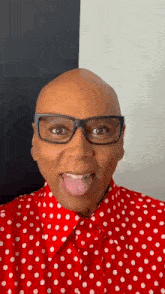 a bald man wearing glasses and a red and white polka dot shirt is sticking his tongue out .