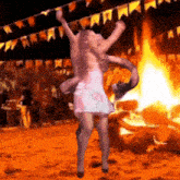 a woman in a pink dress is dancing in front of a large fire