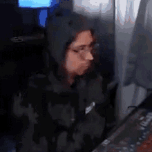 a woman wearing a hoodie and glasses is sitting in front of a keyboard .