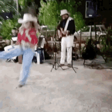 a man in a cowboy hat is playing a guitar while a woman in a cowboy outfit is dancing .