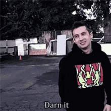 a man wearing a black hoodie is standing in a parking lot and smiling .
