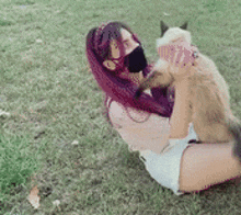 a woman with purple hair is holding a cat in her lap