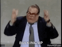 a man in a suit and tie is making a funny face and saying bulking up .