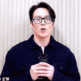 a man wearing glasses and a blue jacket is holding a cup in his hands