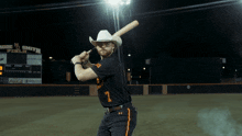 a man in a cowboy hat is swinging a bat at a baseball game