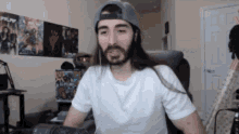 a man with long hair and a beard is wearing a white shirt and a hat .