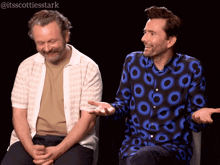 two men are sitting next to each other and one of them is wearing a shirt with circles on it