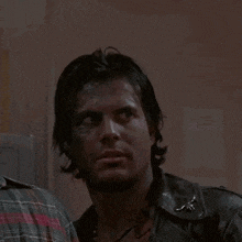 a man wearing a leather jacket and a plaid shirt is looking to the side .