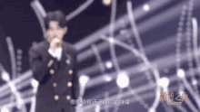 a man in a suit singing into a microphone with chinese writing on the bottom right
