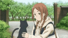 a girl is holding a black cat in her arms while standing in front of a fence .