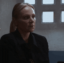 a woman in a black jacket sits in front of a window