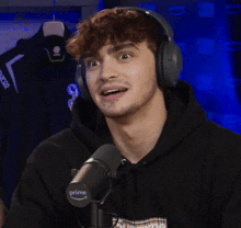 a man wearing headphones and a black hoodie stands in front of a microphone