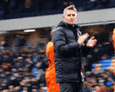 a man in a black jacket applauds the players