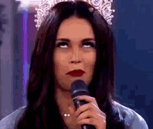 a woman wearing a crown is holding a microphone and making a funny face