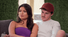 a man in a red hat sits next to a woman in a purple strapless dress