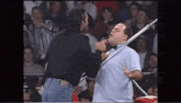 two men are wrestling in front of a crowd and one man is holding a stick in his mouth .