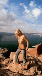 a woman in a bikini is standing on a rocky cliff overlooking a body of water