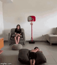 a girl sits in a chair while a boy lays on a bean bag
