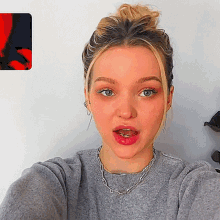 a woman wearing a grey sweater and a silver necklace takes a selfie
