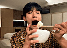 a young man is eating rice with chopsticks from a bowl in a living room .