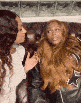 two women are sitting next to each other on a couch and talking .