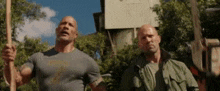 the rock and jason statham are standing next to each other holding a hammer and a stick .