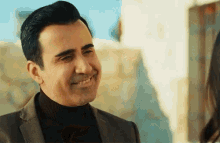 a man in a suit and turtleneck smiles while looking at a woman