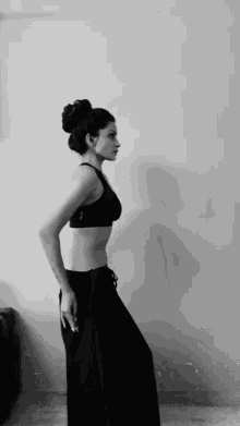 a woman in a black crop top and black pants is standing in front of a wall .