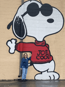 a woman is standing in front of a snoopy mural that says joe cool