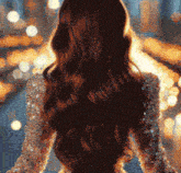 a woman in a dress with long hair is standing in front of a city skyline at night .