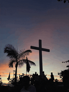 a large cross is silhouetted against a sunset sky with palm trees