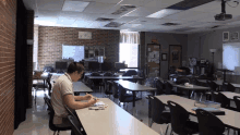 a man sits at a desk in an empty classroom with a sign on the wall that says ' a ' on it