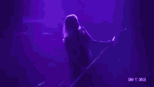 a woman is dancing on a stage in a dark room with purple lights .