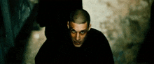 a man with a shaved head is wearing a black shirt and looking at the camera .