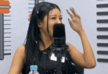 a woman talking into a microphone with a water bottle in front of her