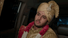 a man wearing a turban and a garland around his neck looks at the camera