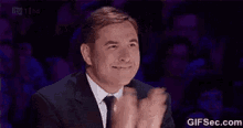 a man in a suit and tie is applauding while sitting in front of a crowd .