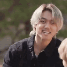 a young man with blonde hair is smiling for the camera while wearing a black shirt .