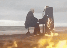a man is playing a piano on the beach with a fire in the background